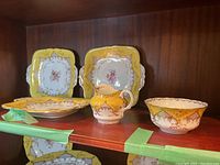 Three square Coalport serving platters with floral and gold decoration on yellow backgrounds, along with matching creamer and sugar bowl.
