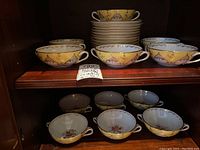 Shelf view showing eleven two-handled cups stacked and displayed with saucers