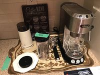 DeLonghi cappuccino machine with glass carafe, Braun coffee grinder, coffee menu chart on decorative tray