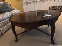 Angle view of round wood coffee table showing curved legs and detailing.