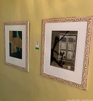 Photo showing both framed photographs hanging on a wall with cream-gold ornate frames and visible shadows