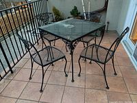 Full view of four black metal patio chairs around glass-top metal table on outdoor balcony