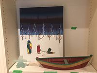 All three items displayed on a shelf: Inukshuk, rowboat and painting