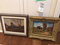 Two framed oil paintings, one with a gray wooden frame and the other with an ornate gold frame, both leaning against a white cabinet.
