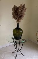 Full view of metal frame round glass top table with large green glass vase and dried pampas grass