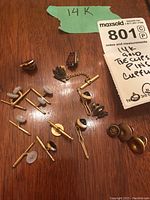 Overview of the lot showing 14K gold cuff links, tie clips and pins laid out on a wooden surface.