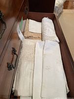 Drawer view showing multiple folded linens in white, ivory and beige, including lace and embroidered pieces