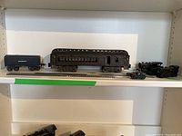 Overview of entire lot on shelf including cast iron coach, metal tender, locomotives, track pieces and coupler