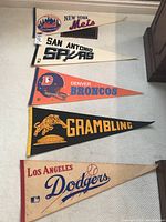 Five vintage sports pennants laid out on the floor showing all pennants in full with visible team names and logos.