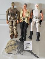Three 12-inch soldier action figures in a row with loose accessories in plastic bag below them