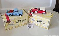 Two Matchbox diecast collectible cars, blue 1955 Chevy Pick-Up and red 1930 vintage car on their original boxes.