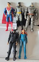 Front view of five DC Comics 12-inch action figures: Superman, Batman, armored Batman, Dark Flash and Mera laid on a flat surface.