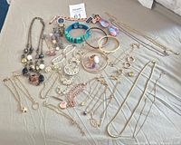 Full view of assorted gold plated and gold tone jewelry spread on surface showing necklaces, bracelets, earrings, a watch, and a turquoise wristband.