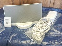 Bose SoundDock Series 1 speaker alongside the white power cord in a plastic bag, all placed on a blue tarp.