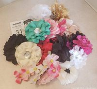 Photo showing a bundle of assorted floral hair accessories including large fabric flower clips in cream, black, teal, pink, red, and gold tones.