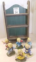 Photo of all six monk figurines arranged in front of the wooden display shelf on a flat surface, showing the entire set
