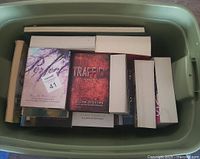 Top view of a green plastic storage bin filled with nine paperback books, showing front covers of two Ellen Hopkins books: PERFECT and TRAFFICK.