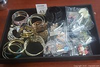 Full view of lot with bracelets, brooches, hair clips and earrings displayed in a black tray.