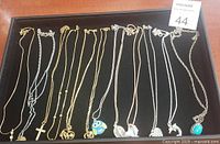 Tray with 12 assorted costume necklaces including various pendants and chain styles in gold and silver tone.