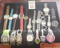 Top view of 19 assorted wristwatches for men and women on black display pad
