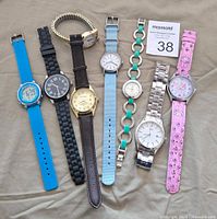 Full view of all seven assorted watches showing various colors and strap types arranged in a row