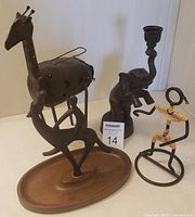 Four vintage home decor figurines including a perforated metal giraffe candle holder, metal and woven man figure, wooden base deer figurine, and metal elephant candle holder.