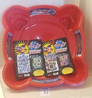 Red plastic Beyblade stadium with four sealed Beyblade Punch-Out & Build Spinners sets placed inside compactly.