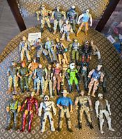 Full lot of approximately 28 military action figures arranged on patterned fabric chair showing overall quantity and variety.