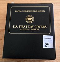 Photo showing front cover of the black binder album with title 'Postal Commemorative Society U.S. First Day Covers & Special Covers' with seller auction lot tag number 29.