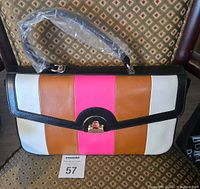 Front view of Trina Turk handle bag showing colorblock leather pattern with white, brown, pink and black accents and single handle wrapped in plastic.