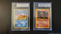 Front of two graded Pokémon cards, Krabby (7.5) on left and Magmar (7.0) on right, in clear plastic cases.