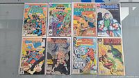 Full view of 8 DC Comics comics laid out on table, showing front covers with bright colors and mostly intact condition, bagged and boarded.