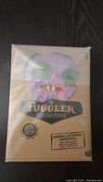 Front view of sealed Fuggler bunny plush toy box, showing purple bunny face with green stitched eyes and teeth