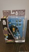 Full boxed view of the Ninja Turtles BST AXN Leonardo action figure including accessories in clear plastic packaging.