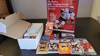 Photo showing red Tim Hortons 2021-2022 NHL trading cards binder, box of loose hockey cards, and several cards laid out on table.