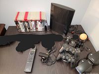 Sony PlayStation 3 console, three controllers, remote control, PlayStation Eye camera, and various cables arranged on a dark surface.