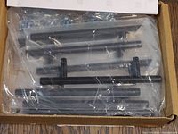 Box containing 10 flat black cabinet handles in sealed plastic bags inside box.