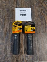 Two DeWalt deep impact sockets with yellow and black labels indicating sizes 16mm and 5/8" SAE and 1/2" drive, set on wooden surface with lot number card