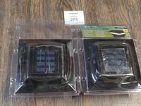 Two black solar post caps each with a solar panel in the center, shown side by side on a wooden surface.
