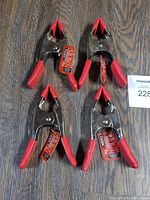 Four new TASK brand 2 inch spring clamps laid on wood surface, showing their red handles and tips.