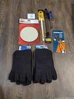 Photo from above showing five tools and two pairs of black toe socks work gloves arranged on wooden floor.