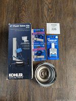 Photo shows 5 new plumbing and home maintenance items including Kohler 2" flush valve kit, metal sink strainer basket, toilet repair kit with faucet cartridges, and Mr. Touch-Up appliance white touch up paint.
