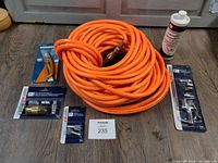 Photo showing entire lot with orange Husky air hose coiled in center, Campbell Hausfeld compressor oil bottle on the right, Starkman utility knife with yellow handle on left, and multiple packaged fittings from Campbell Hausfeld surrounding the hose on a wooden floor.