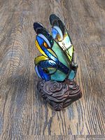 Close-up image of blue and green stained glass butterfly wing with bronze rose base on wood surface
