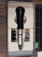 View inside the metal case showing the black handled setter tool and six metal bits in foam insert