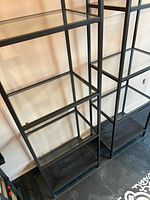 Close-up photo showing the glass shelves within black metal framed shelving units, highlighting the construction and material of the shelves.