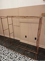 Full view of both copper pipe shelving frames together, showing rectangular structure and multiple horizontal bars for supporting shelves.