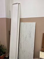 Two white painted pine wood shelves standing vertically next to a faux marble table top leaning against a wall.