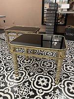 Two rectangular brass-framed side tables with black glass tops on patterned floor