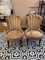 Front side view of two vintage slipper chairs showing brown velvet fabric with wear and stains, upholstered rounded backs with vertical channel tufting, seated on wooden legs with casters under.